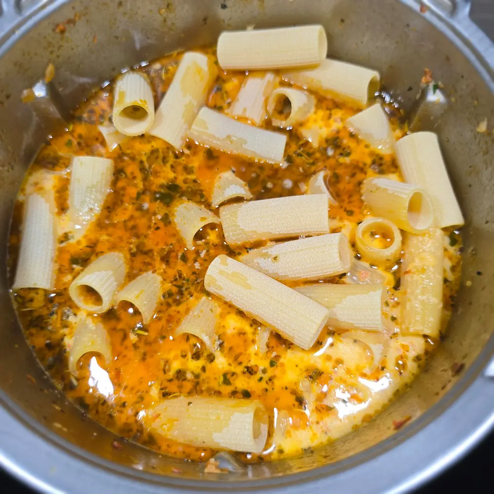 Surowy makaron rurki dodany do pomarańczowego sosu z ziołami w naczyniu Thermomix