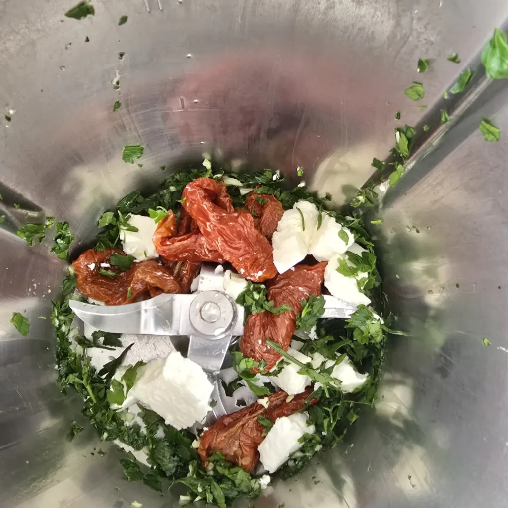 Suszone pomidory z fetą i pietruszką w naczyniu Thermomixa przed miksowaniem